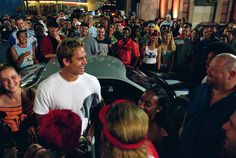 a man standing in front of a car surrounded by people and talking to each other