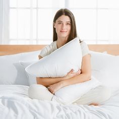 a woman sitting on top of a bed with pillows in her lap and smiling at the camera