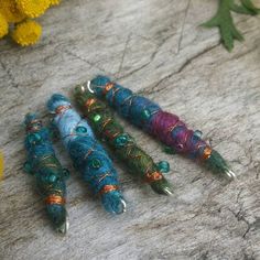 four different colored beads sitting on top of a table next to yellow flowers and leaves