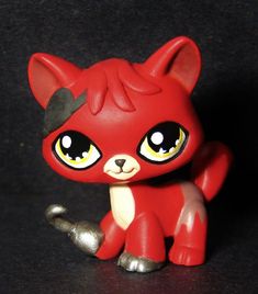 a small red toy with big eyes sitting on a black surface next to a silver object