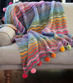 a multicolored knitted blanket with pom - poms sitting on a couch