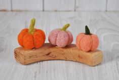 three small felt pumpkins sitting on top of a wooden stand, one orange and one pink