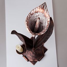 a metal object with an open flower on it's top and a candle holder in the middle