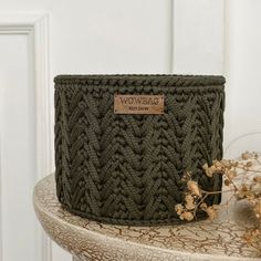 a green knitted basket sitting on top of a table next to dried flowers and a white door