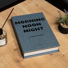 a book sitting on top of a wooden table next to a candle and potted plant