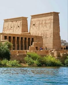 two large stone buildings sitting on the side of a body of water next to trees