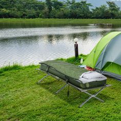 a green tent sitting on top of a lush green field next to a lake