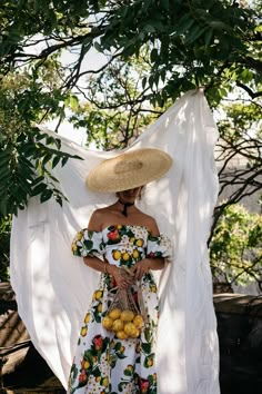 a woman wearing a straw hat and dress standing in front of a white cloth draped over her head