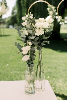 two vases filled with flowers on top of a table in the middle of a field