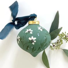 a green ornament with white flowers on it and a blue ribbon hanging from the top