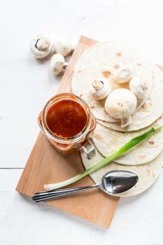 some food is sitting on a cutting board with spoons and a jar filled with sauce