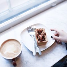 a person holding a fork and knife over a plate with food on it next to a cup of coffee