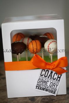 a white box filled with cake pops covered in chocolate and orange frosted baseballs