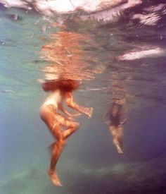 two people are swimming in the water with their backs turned to the camera, and one person is holding a book