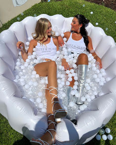 two women sitting in an inflatable bubble filled pool with white balls on the ground