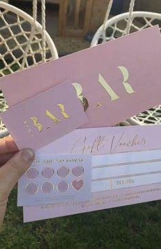 someone holding up two pink and gold gift cards