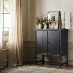 a wooden cabinet sitting next to a window in a room with curtains and a rug on the floor