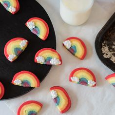 there are rainbow cookies on the table next to a glass of milk and a black plate