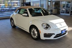 a white car parked in a showroom with lots of windows and blinds behind it