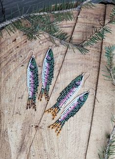 three beaded earrings sitting on top of a piece of wood next to pine needles