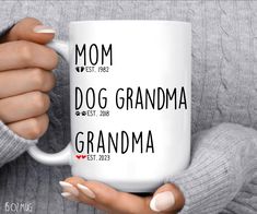 a woman holding a white coffee mug with the words'dog grandma'on it