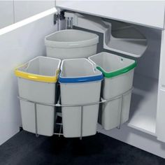 three plastic trash cans in the corner of a white cabinet with yellow, blue and green handles