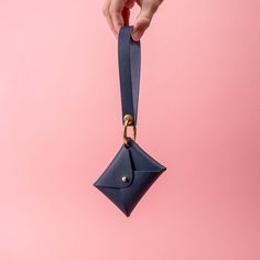 a hand holding a small blue purse on a pink background