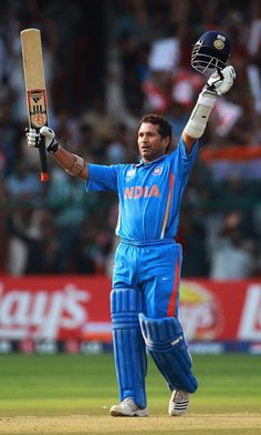 a cricket player holding his bat up in the air while standing on top of a field