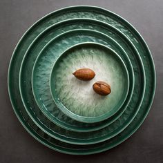 three green plates with nuts on them sitting on top of each other in front of a black table