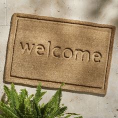 a welcome mat with the word welcome written on it next to a potted plant