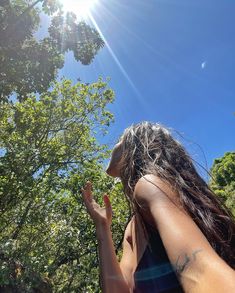 a woman with long hair standing in front of trees and looking up at the sky