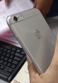 a person holding an iphone in their hand next to a keyboard and computer mouse on a desk