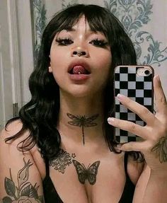 a woman taking a selfie with her cell phone in front of her face and tattoos on her chest