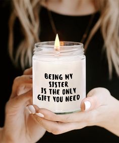 a woman holding a candle that says being my sister is the only gift you need