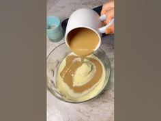 someone is pouring something into a bowl with some liquid in it and another cup on the table