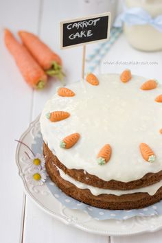 carrot cake with frosting and icing on a plate next to fresh carrots