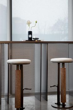 two stools sitting next to each other in front of a table with a vase on it