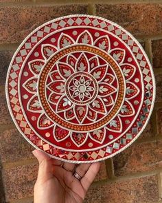 a hand holding a red and white plate with an intricate design on the bottom, in front of a brick wall