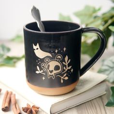 a black coffee mug sitting on top of a table next to cinnamons and leaves