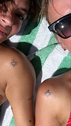 two women laying on top of a towel next to each other with tattoos on their backs