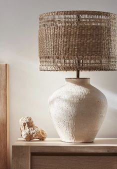 a white vase sitting on top of a wooden table next to a brown lamp shade