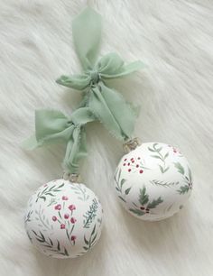 two white ornaments with green bows on them sitting on a fur covered floor next to each other