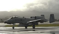 a fighter jet sitting on top of an airport tarmac with mountains in the background