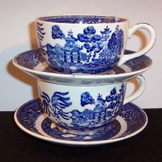 two blue and white tea cups with saucers on each one, sitting side by side