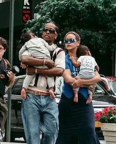 a man and woman walking down the street with two children on their shoulders, one carrying a baby