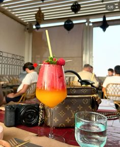 a drink sitting on top of a table next to a camera and other people in the background