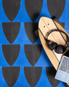 a surfboard, headphones and laptop computer on a blue and black tile background