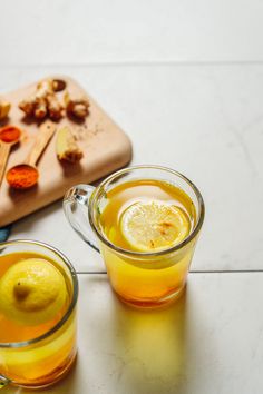 two glasses filled with lemon tea next to a cutting board