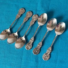 six silver spoons are lined up on a blue cloth