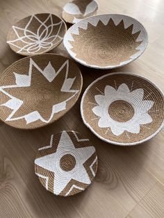 four woven baskets with designs on them sitting on a wooden floor in front of a wall